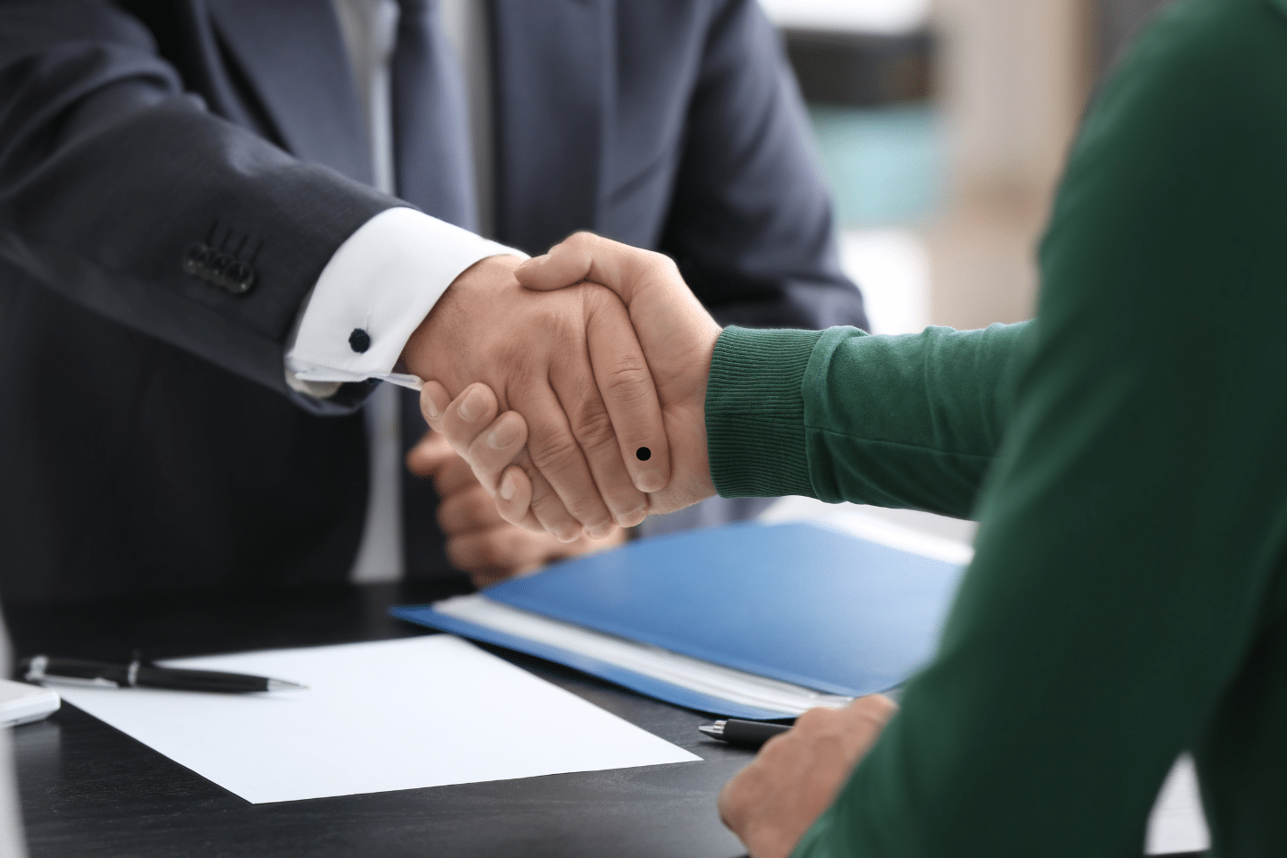 Two people shaking hands across a desk to finalize a business agreement.