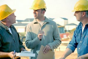 Purchase a surety bond - The image shows three contractors discussing and wearing a yellow hard hat.