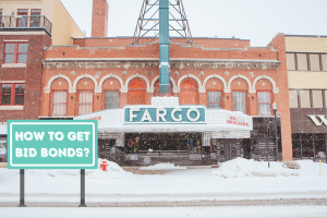 Historic Fargo Theater in North Dakota covered in snow, featuring a sign that says 'How to Get Bid Bonds?'. A step-by-step guide to obtaining bid bonds in North Dakota.