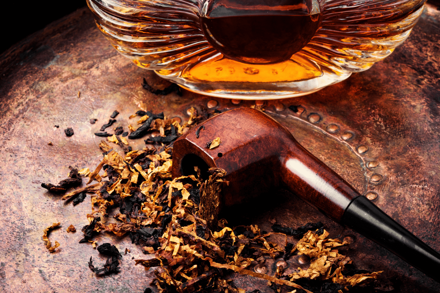 A wooden smoking pipe and loose tobacco sit beside a decanter of amber liquor.