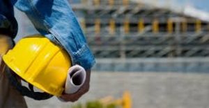 California Bid Bonds - A contractor holding a yellow hard hat infront of a constructed building.