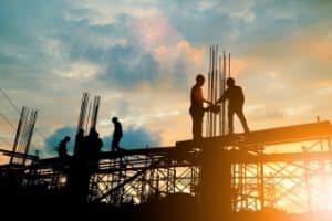 Construction surety bond - The image shows a contractors working in a construction site with a cloudy sky ang a sun as the background.