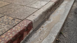 Damaged sidewalk curb in San Antonio, Texas illustrating public infrastructure protected by contractor bonding.