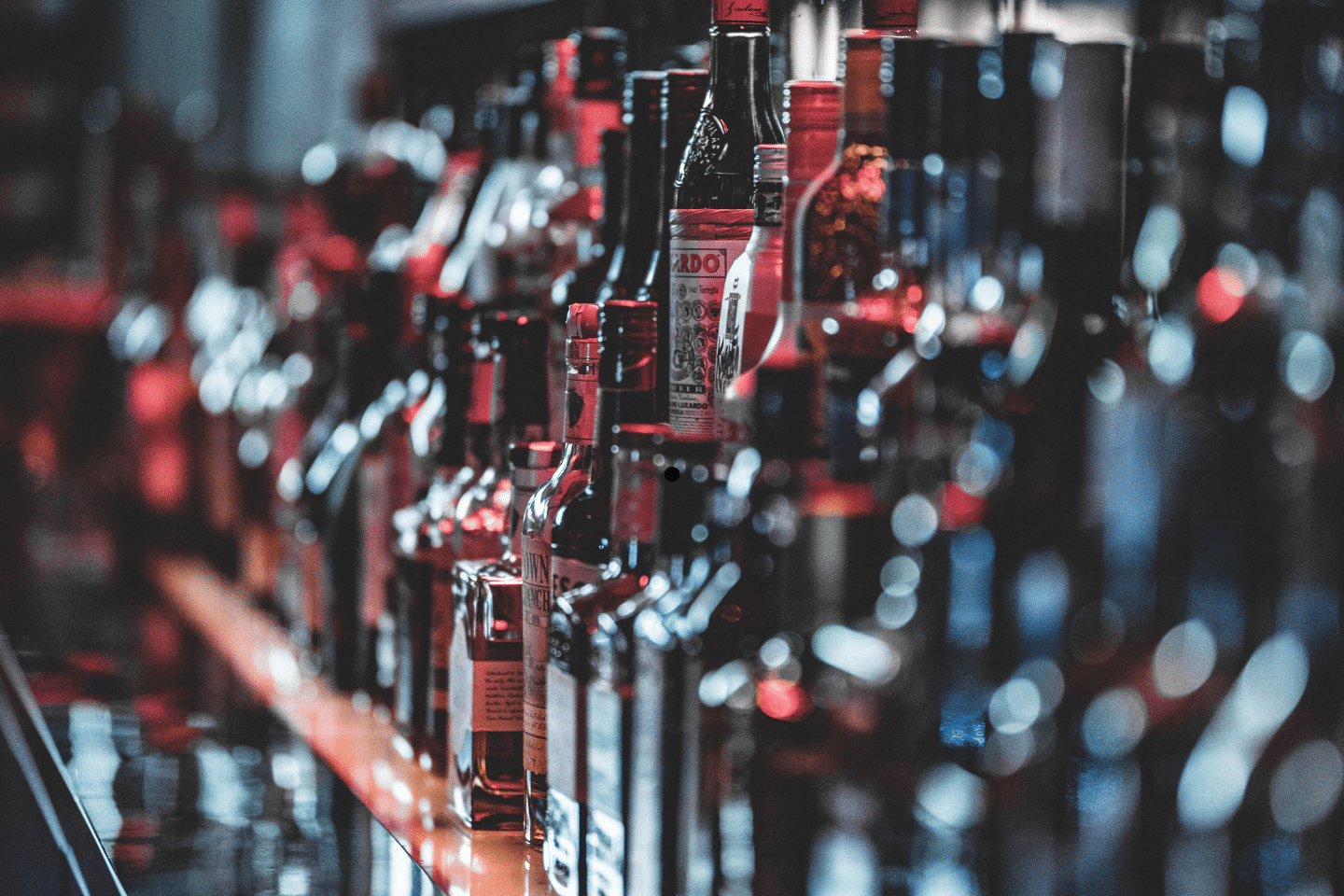 A blurred row of assorted liquor bottles displayed on a bar shelf.
