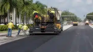 Road construction workers operating paving machinery during a roadway restoration project covered by an Escambia County, FL Road Restoration Permit Bond.