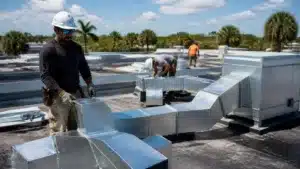 HVAC installer positioning galvanized ductwork on a commercial building rooftop