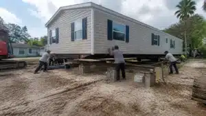 Workers moving a manufactured home onto foundation supports as part of a Florida trailer placement project.