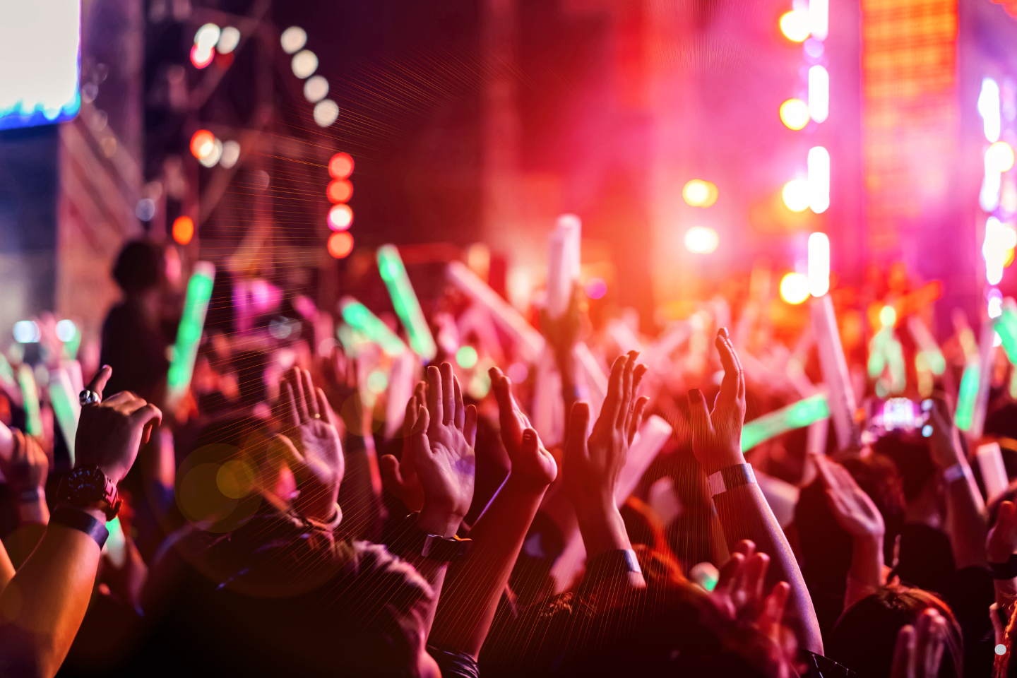 A vibrant nighttime concert scene with colorful lights and raised hands in the audience.