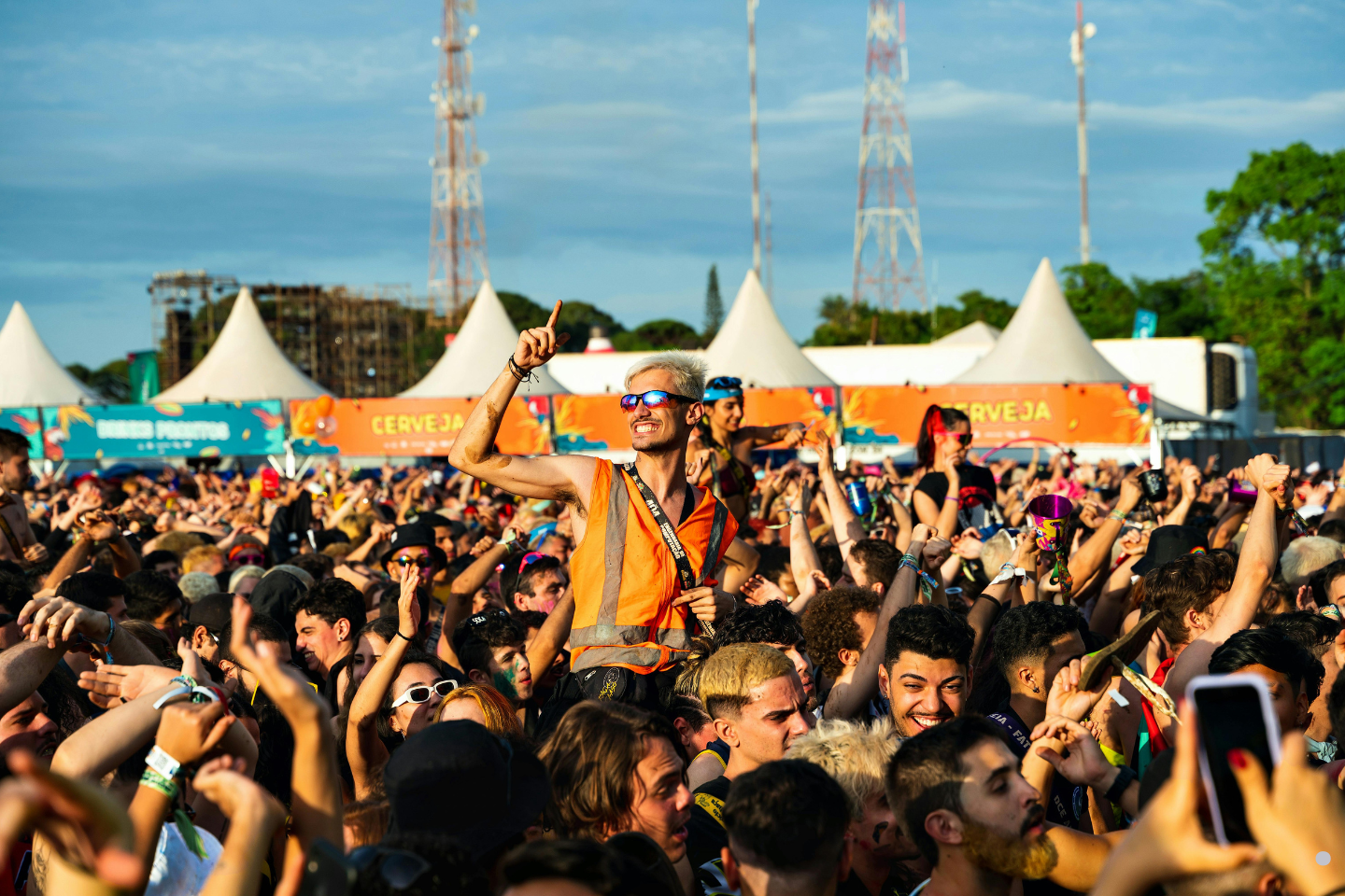 A lively outdoor festival crowd with people cheering and dancing under bright daylight.