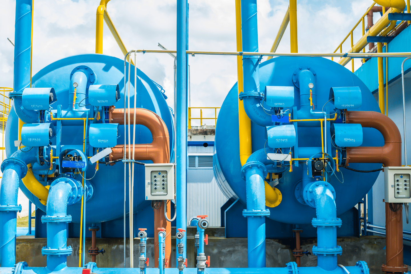 Dual blue industrial filtration tanks connected by multiple colored pipes and valves.