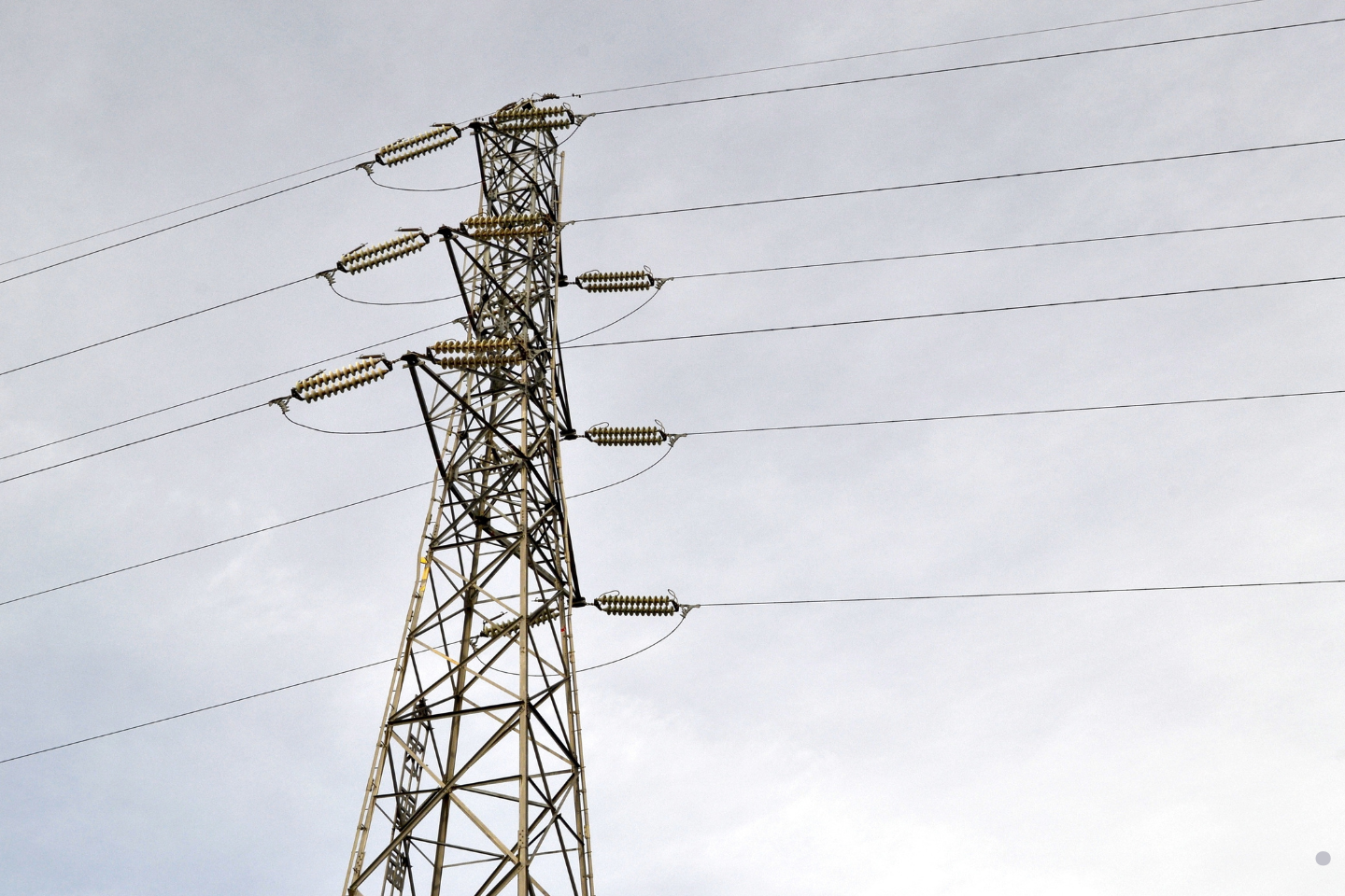 High-voltage transmission tower with multiple power lines against an overcast sky.