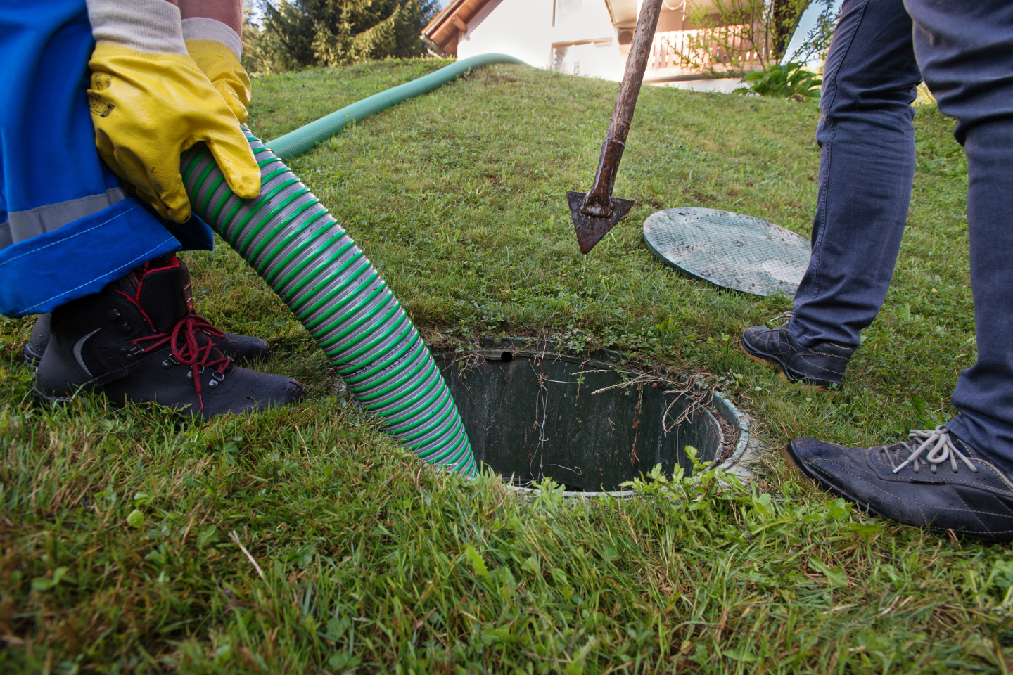 Worker using a large suction hose to pump out a septic tank in a grassy yard.