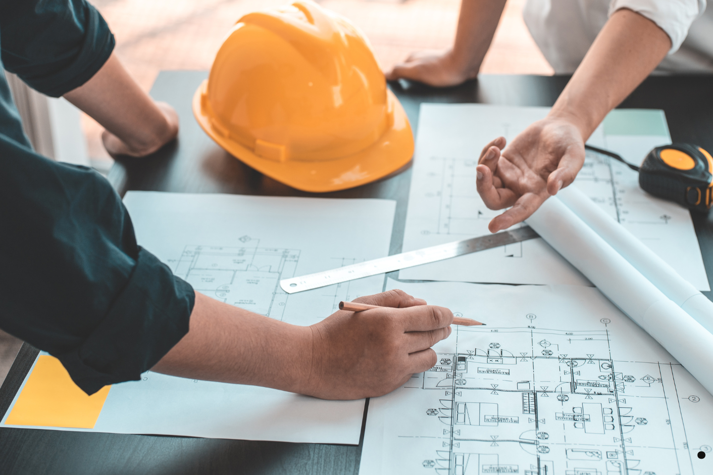 Construction professionals reviewing blueprints and plans with a hard hat on the table.