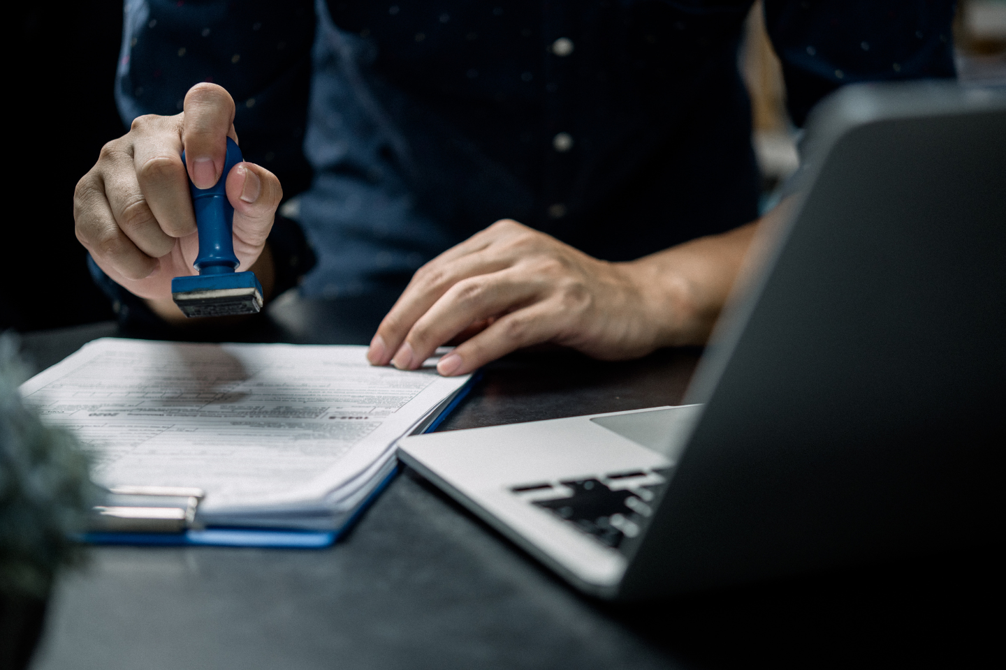 A person stamping official documents on a clipboard beside an open laptop.