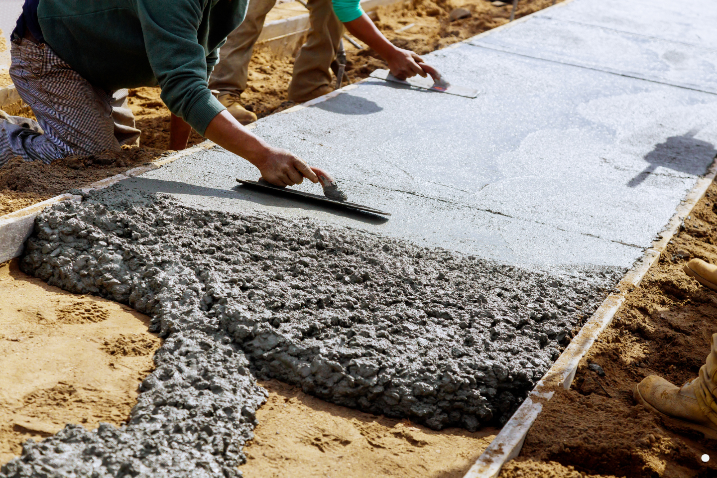 Contractors smoothing freshly poured concrete on a walkway using hand trowels.