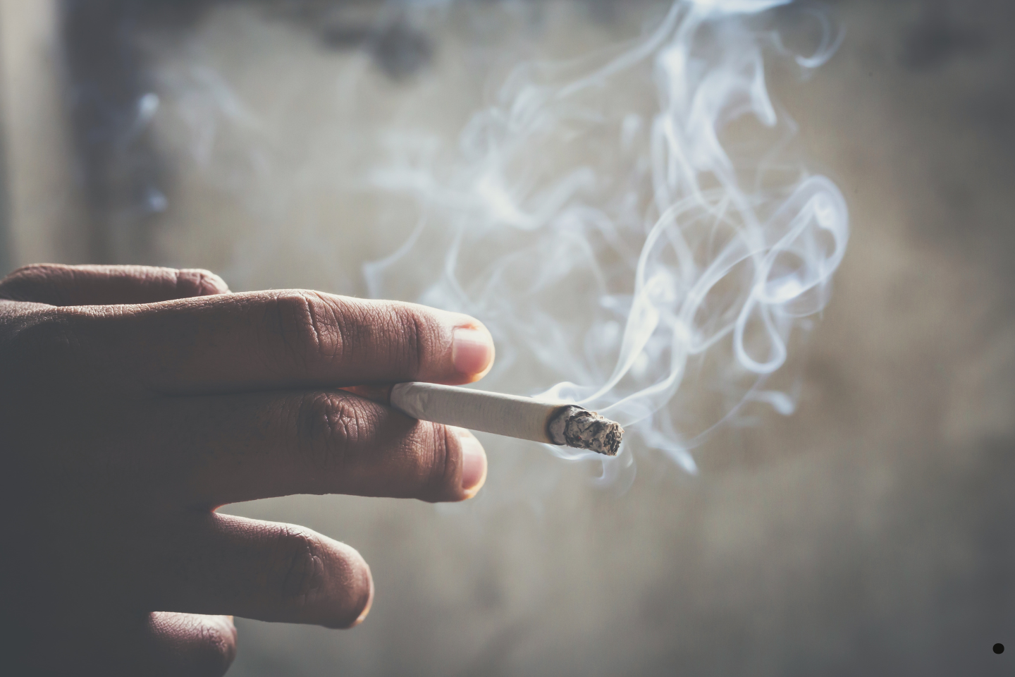 A hand holds a lit cigarette with smoke curling upward.