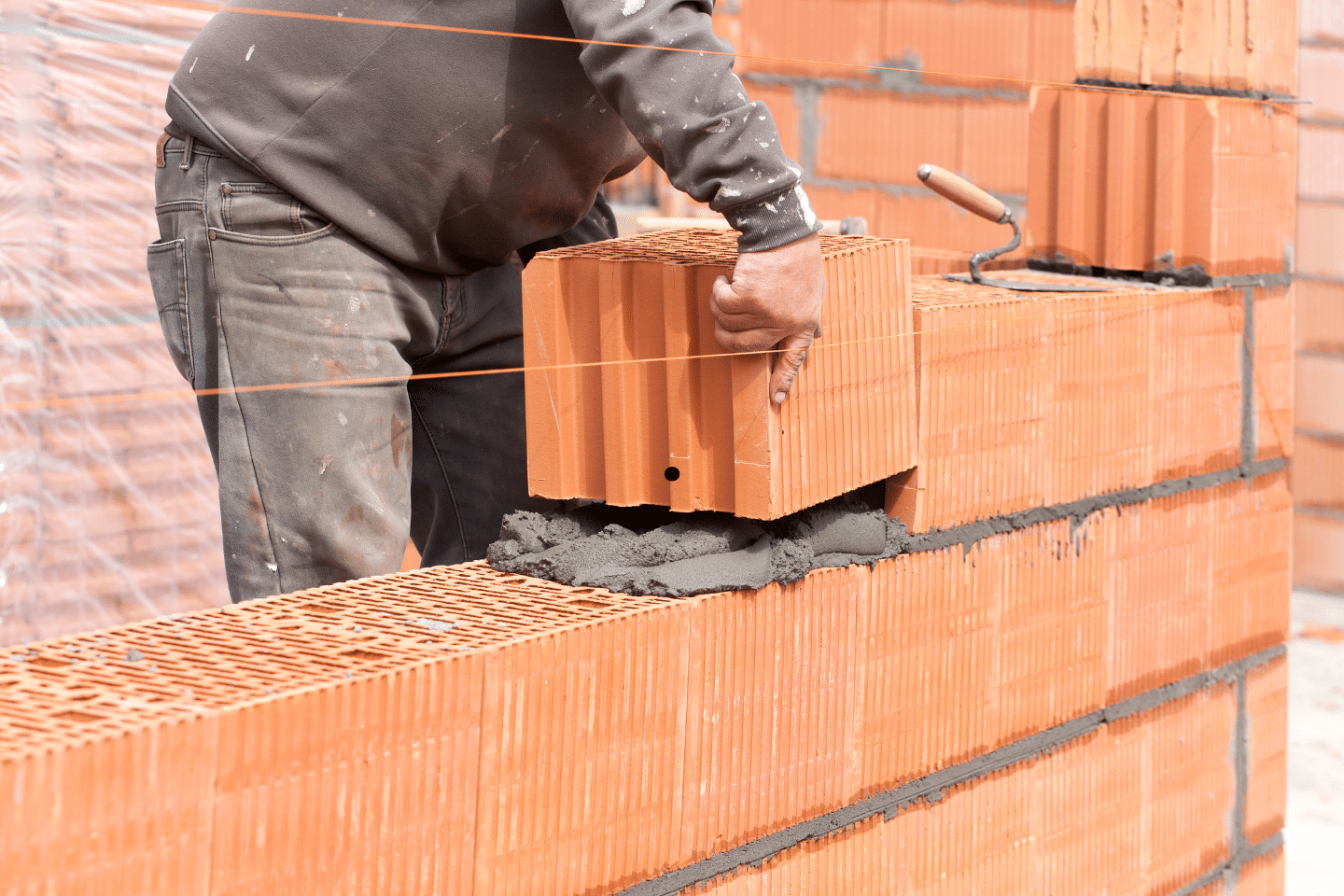 A bricklayer placing a large clay block onto fresh mortar while constructing a wall.