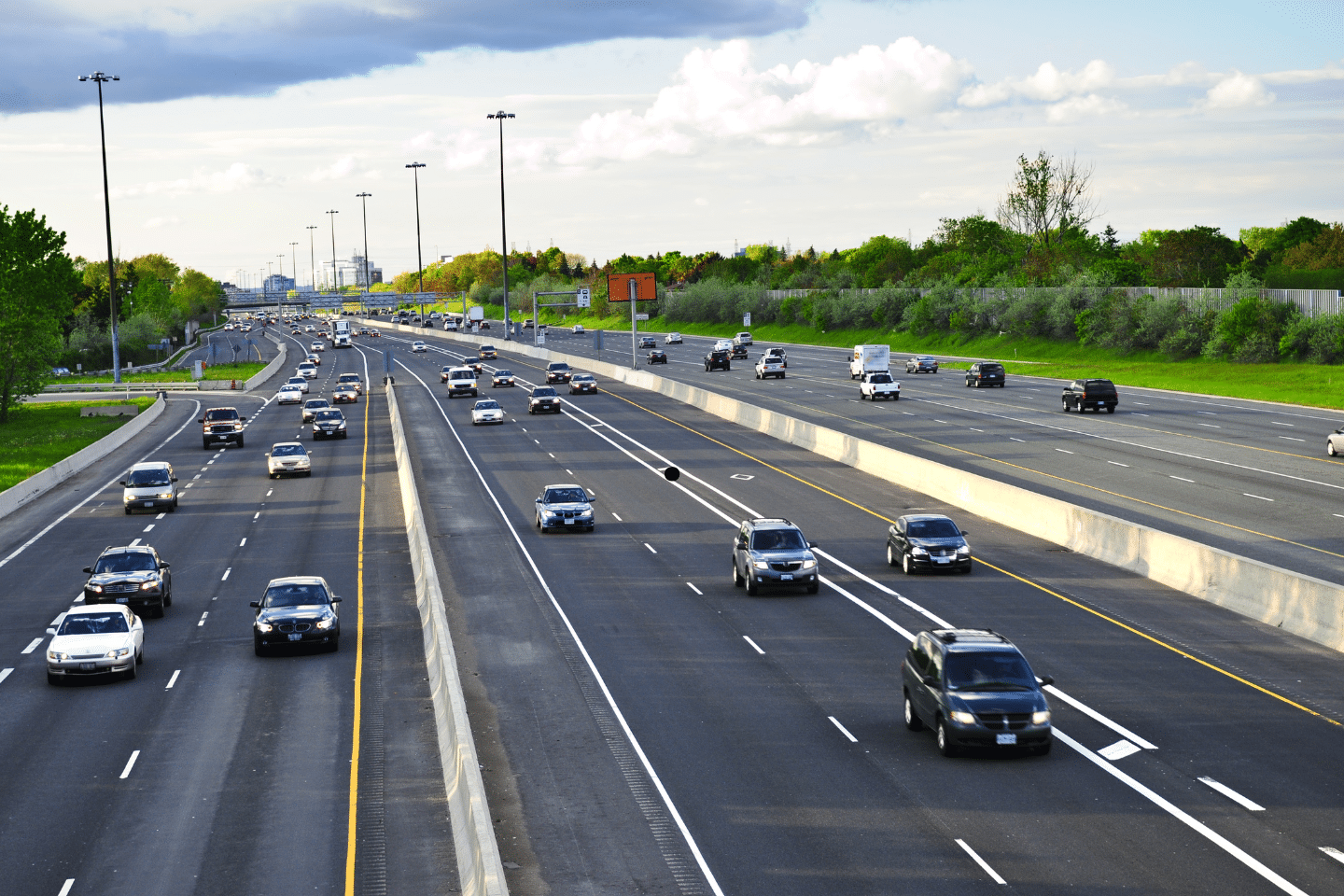 Multiple-lane interstate with steady traffic under bright daylight and scattered clouds.