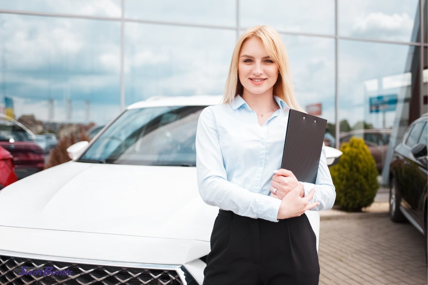 An employee from a car dealership stands in front of a car at the workplace.