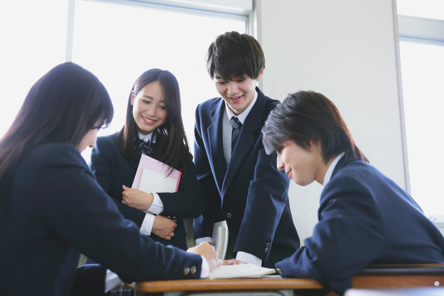 A group of high school students in uniforms collaborating and smiling during classwork.