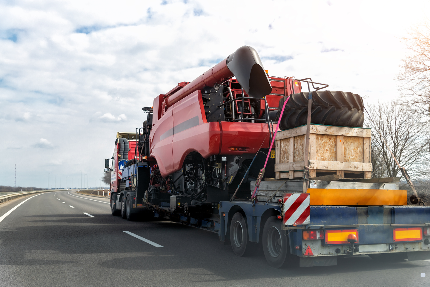 Oversized agricultural machinery secured on a flatbed truck traveling on a highway, illustrating regulated hauling under temporary permits.