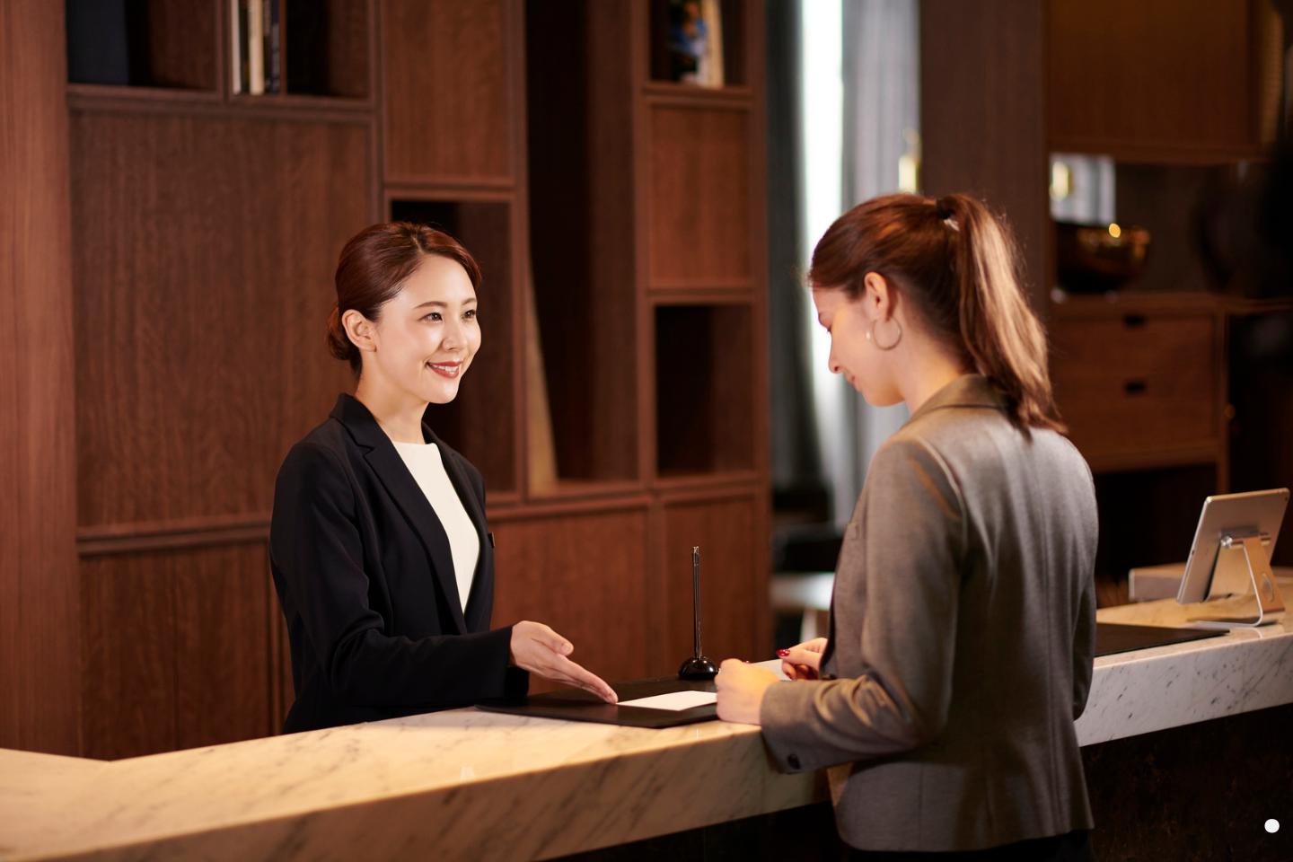 Hotel receptionist smiling while assisting a guest at the front desk.