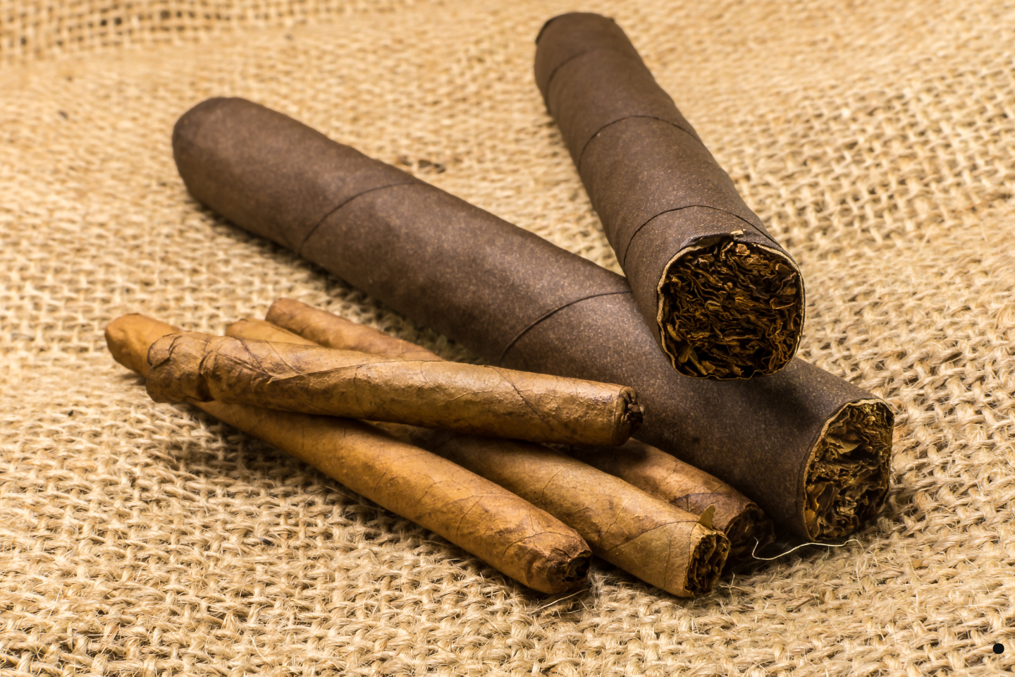 Several cigars and tobacco leaves arranged on a burlap surface.