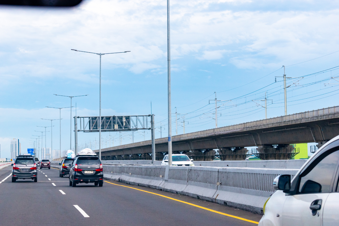 Cars traveling along a multi-lane highway beside an elevated rail line.