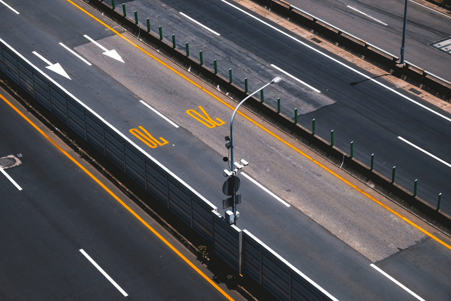Empty multilane highway with directional markings and barriers under bright sunlight.