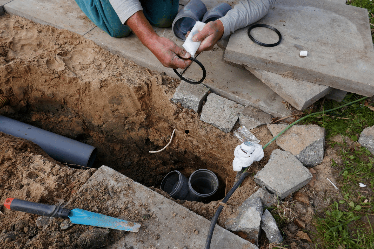 Contractor repairing underground sewer pipes and fittings in a dug-out area.