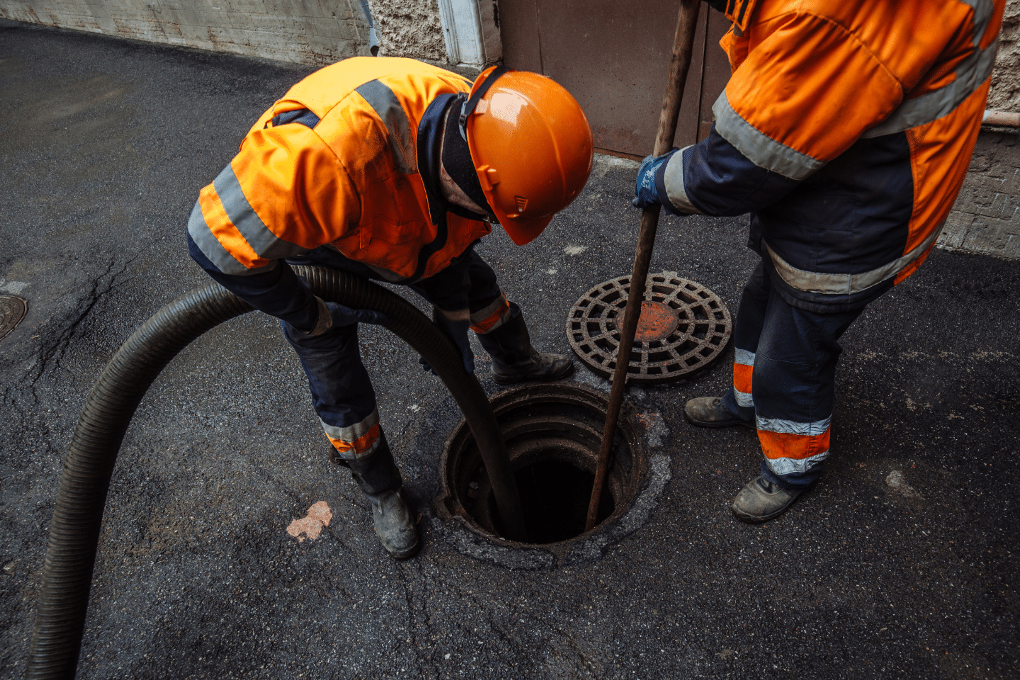 Workers in safety gear cleaning and inspecting a sewer manhole with industrial equipment.
