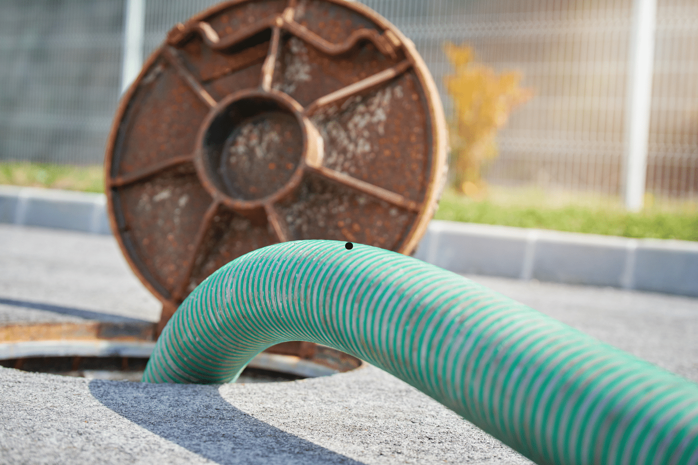 A large green hose extending from an open manhole with a rusty cover nearby.