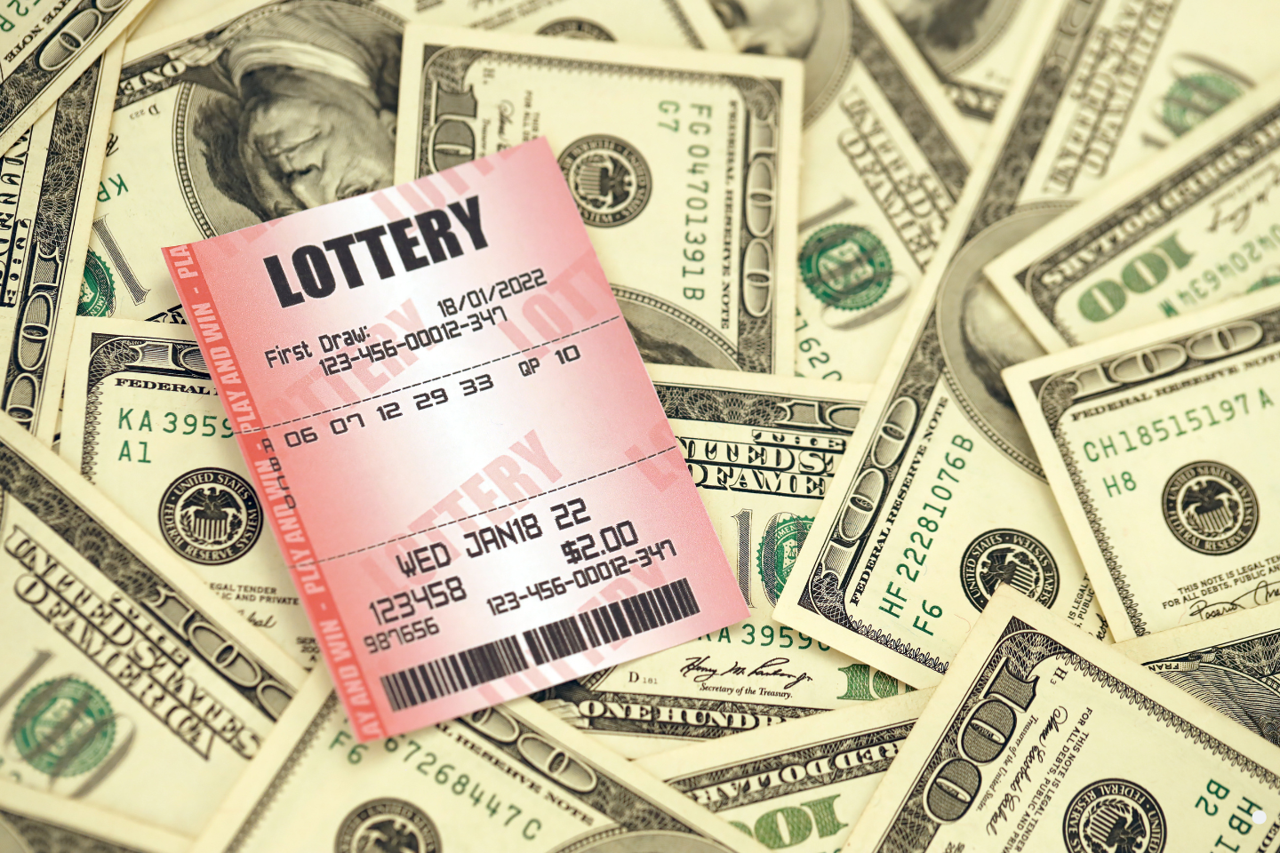 A lottery ticket placed on top of scattered U.S. dollar bills.