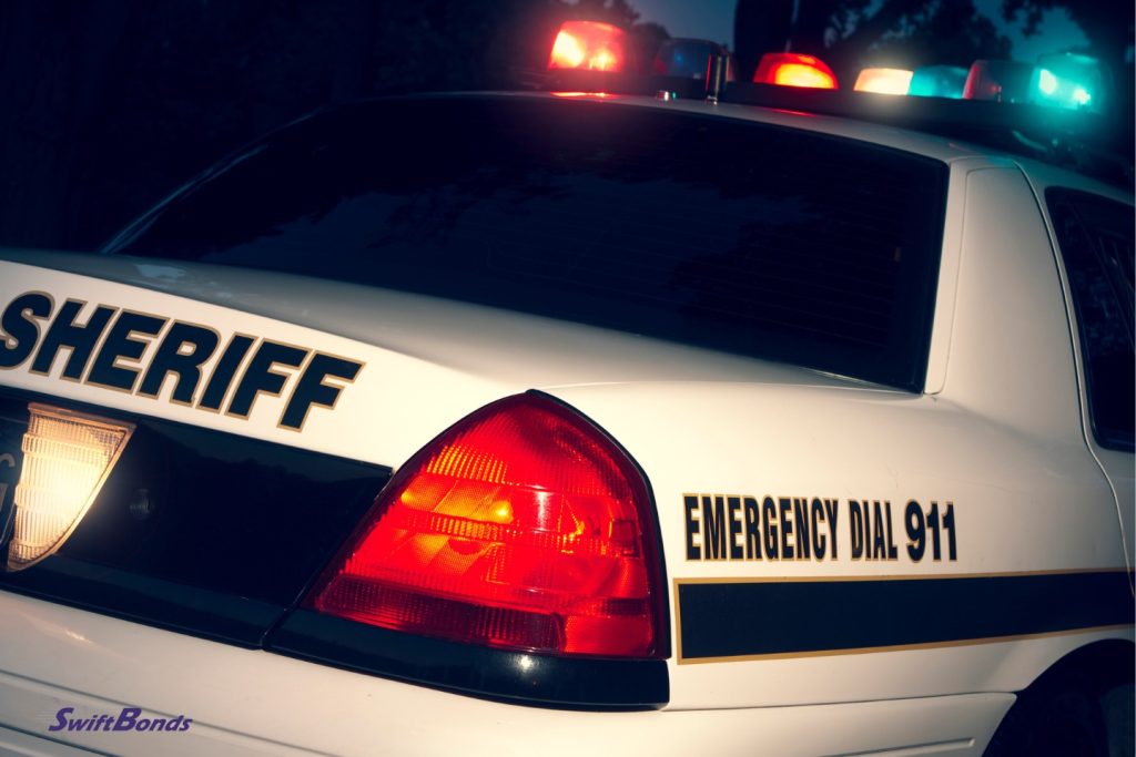 A sheriff at the crime scene. The car's top lights are flashing.