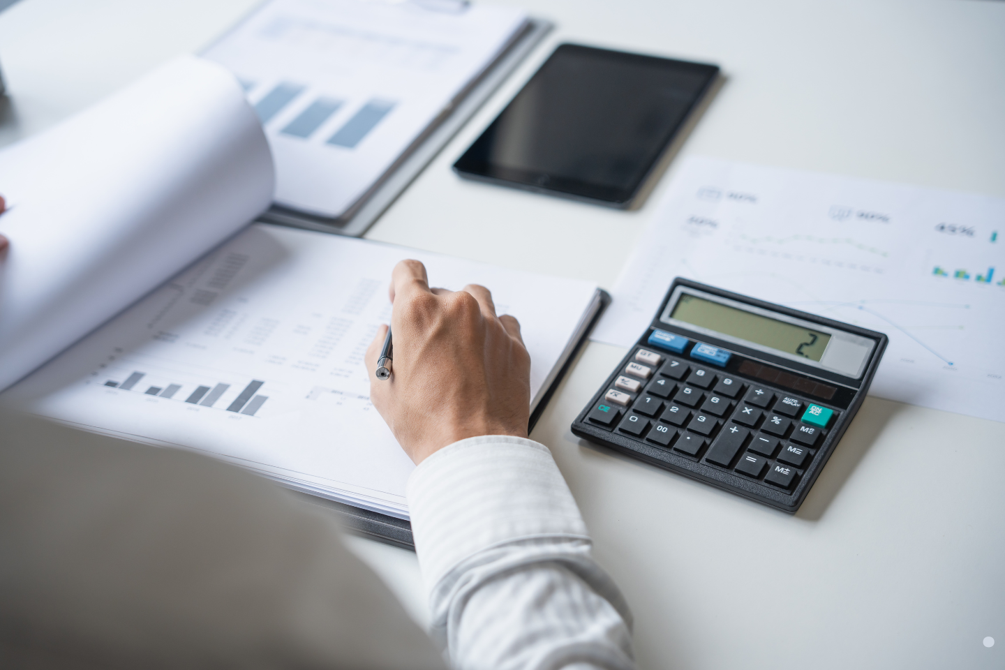 Accountant reviewing reports with a calculator and charts on a desk, illustrating financial analysis tied to surety bond oversight.