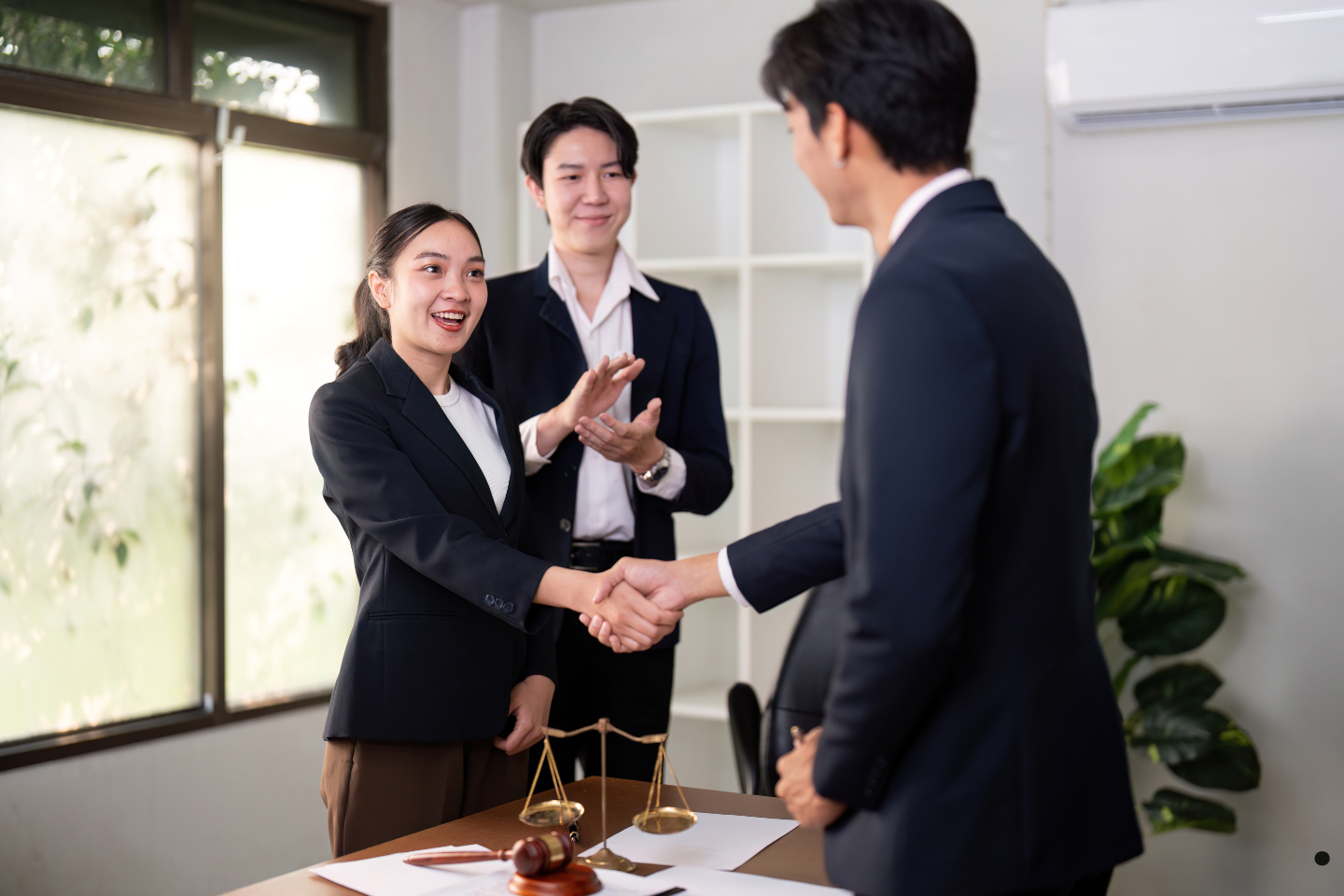 Three professionals in an office celebrating as two of them shake hands.