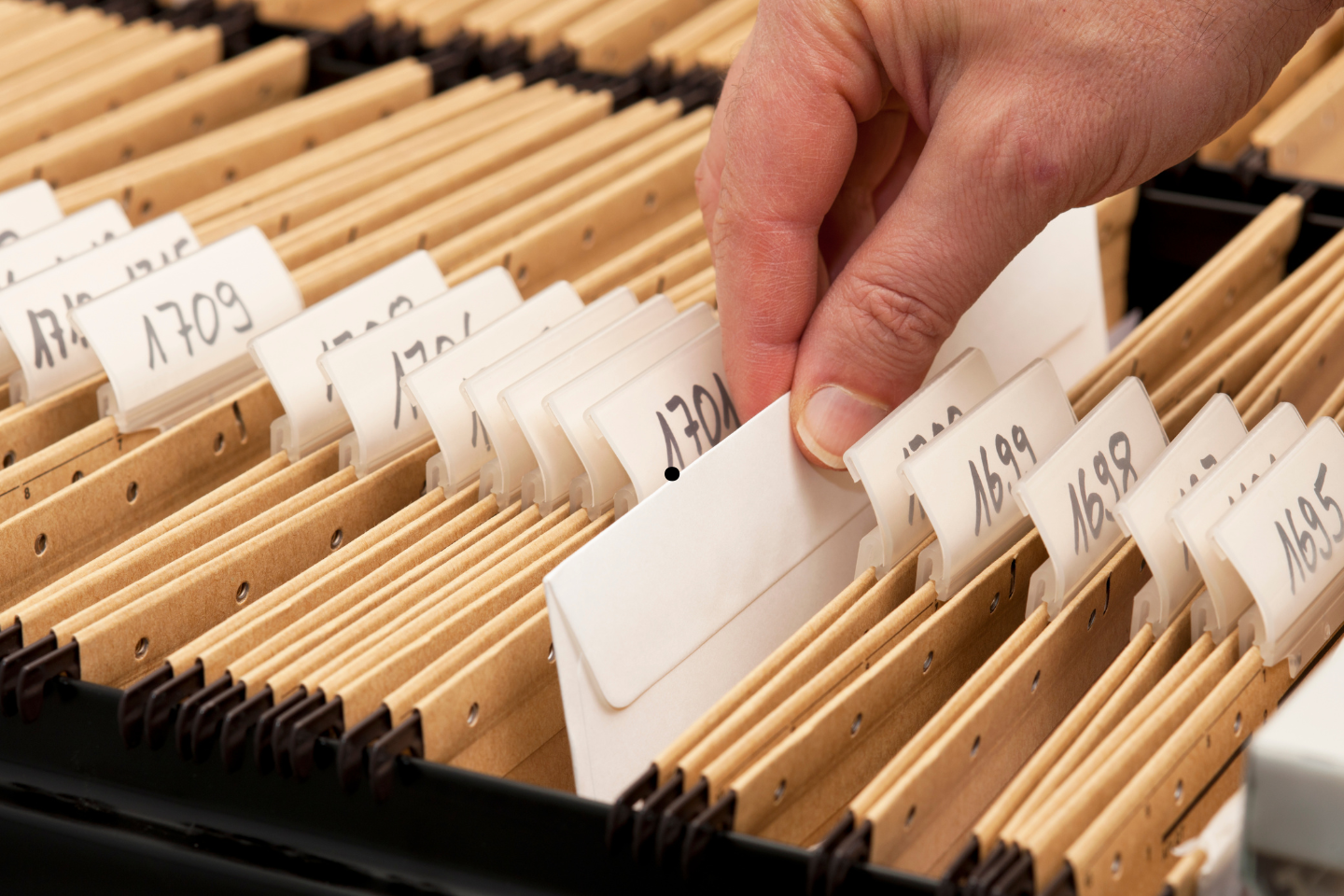 Hand selecting a labeled file from an organized filing drawer.