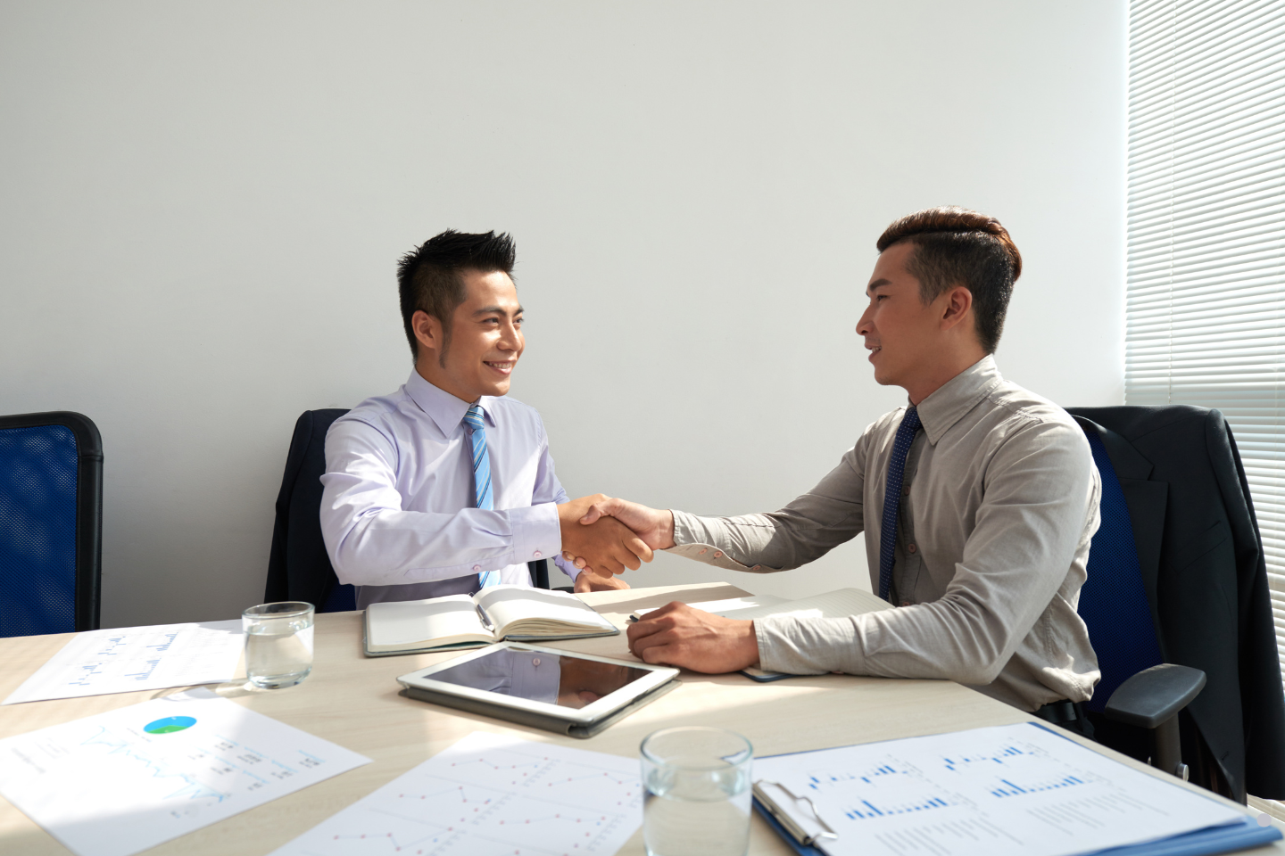 • Two businessmen shaking hands across a table during a meeting.