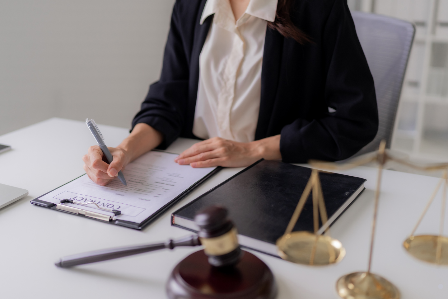 A professional signing a contract at a desk with a gavel and scales of justice nearby.