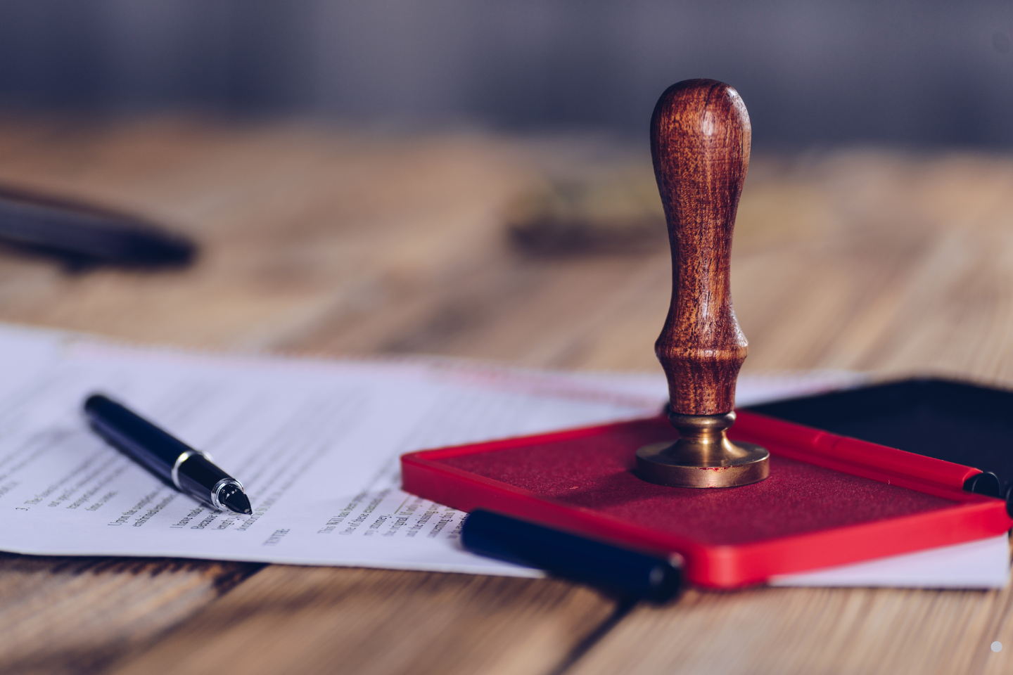 A wooden notary stamp and pens resting on top of legal paperwork.