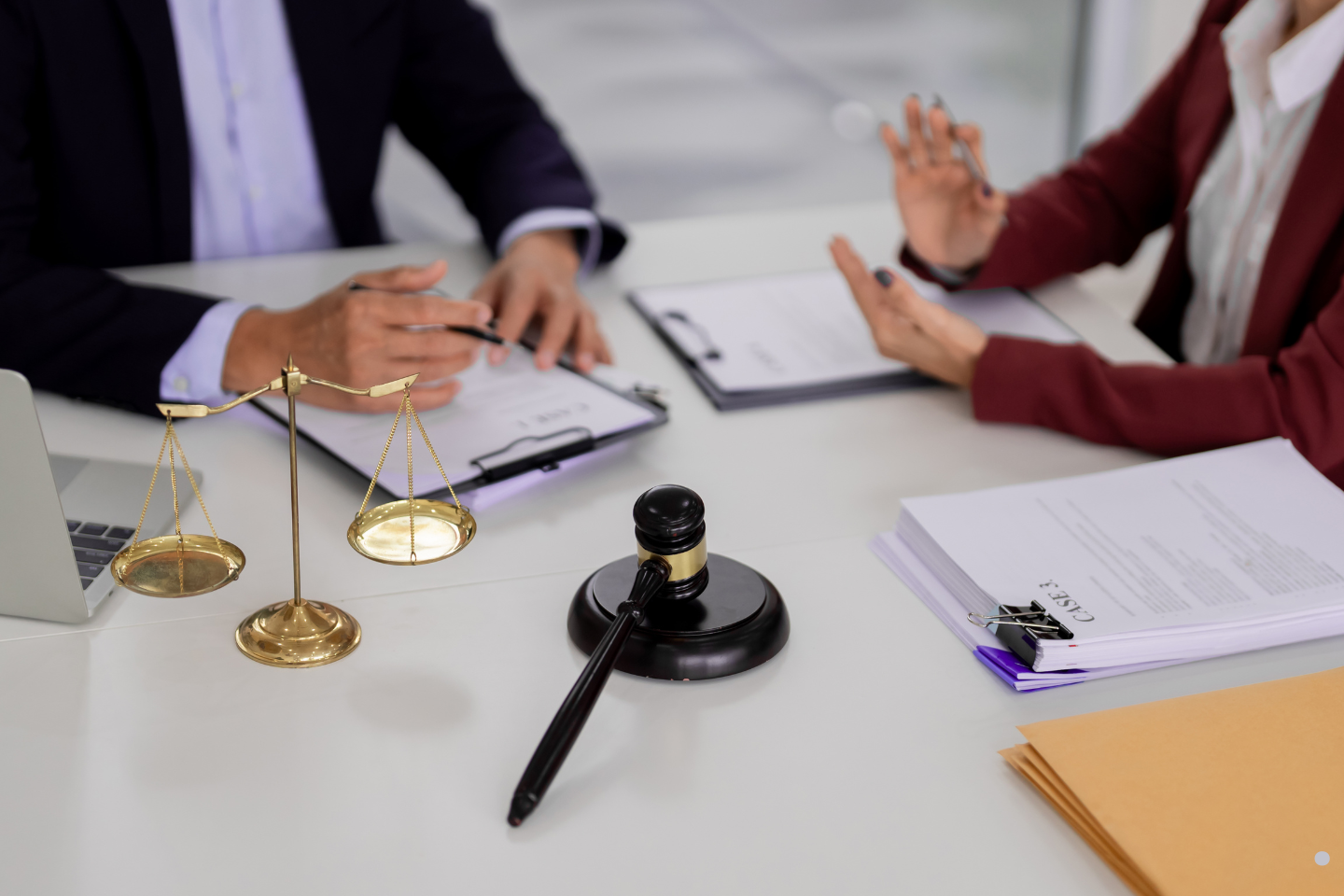 A gavel and scales of justice sit on a desk as two people discuss documents.