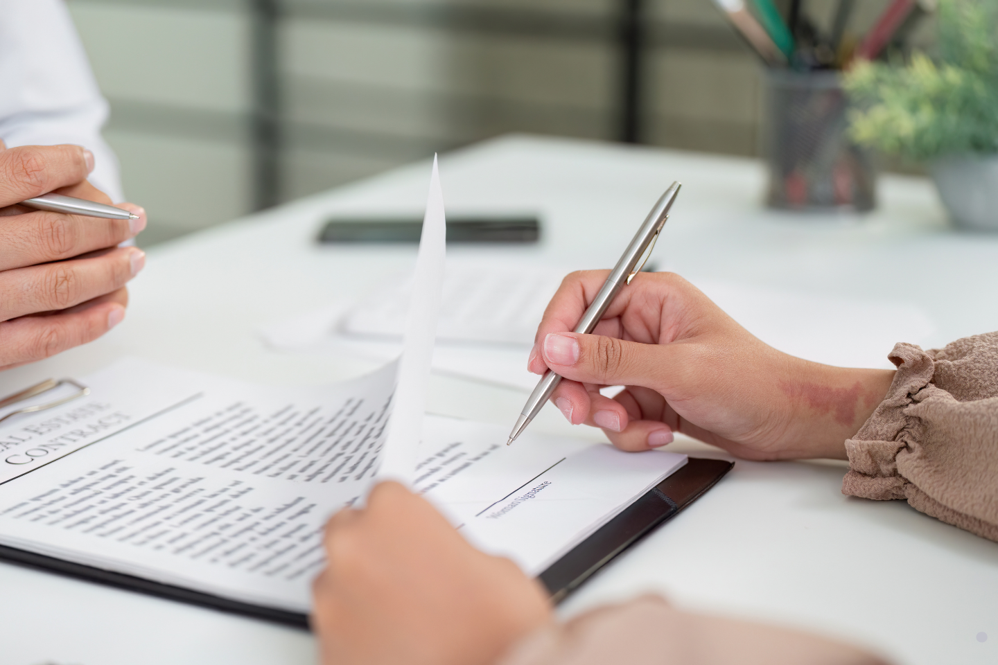 A person reviews and signs a contract while flipping through its pages at a desk.