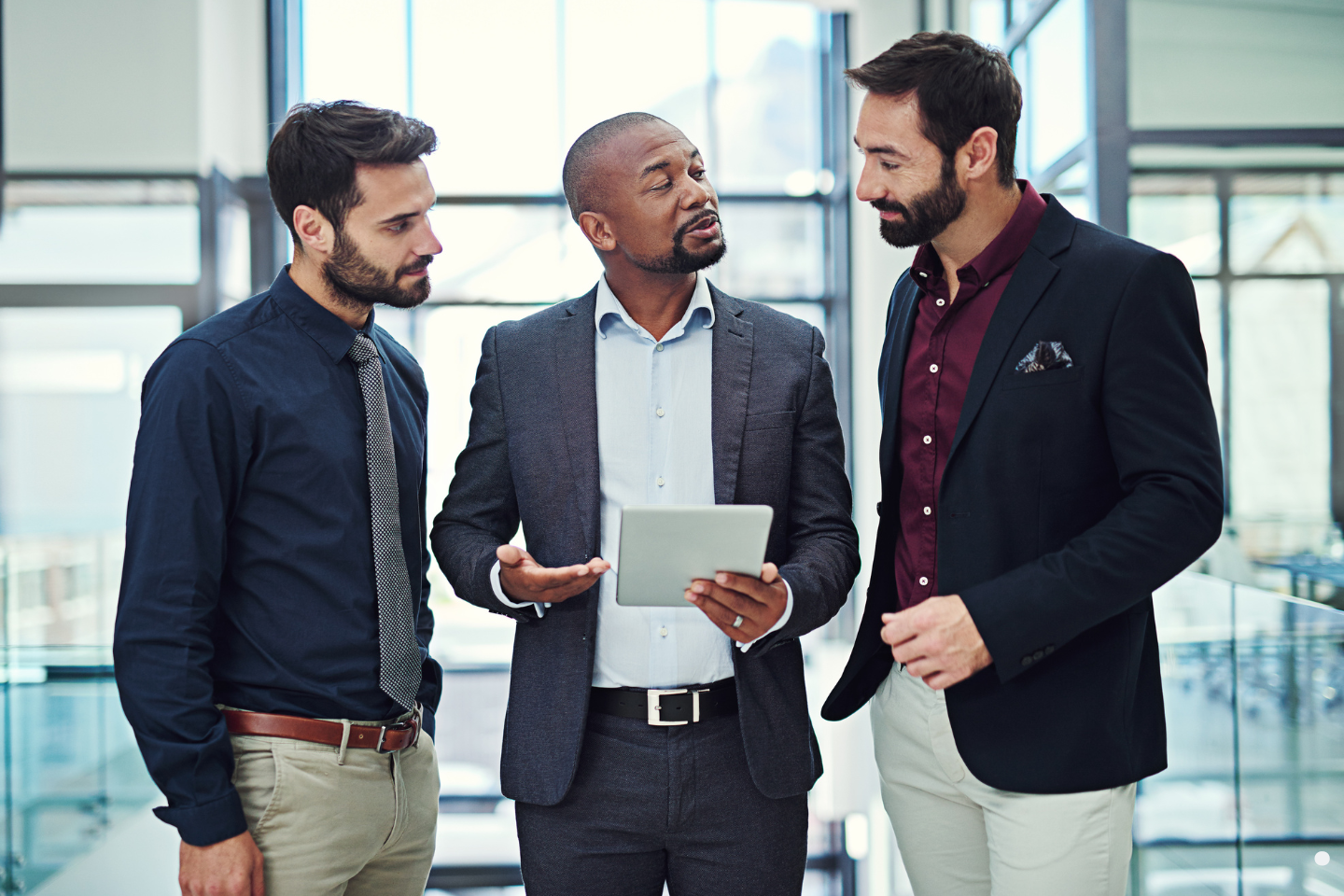 Three businessmen having a discussion while one holds a tablet.