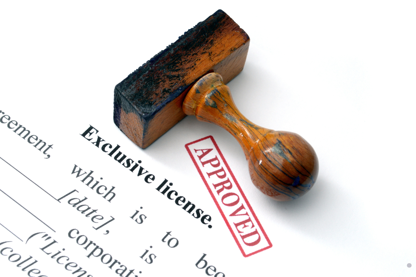A wooden approval stamp resting on a document marked with a red “APPROVED” stamp.