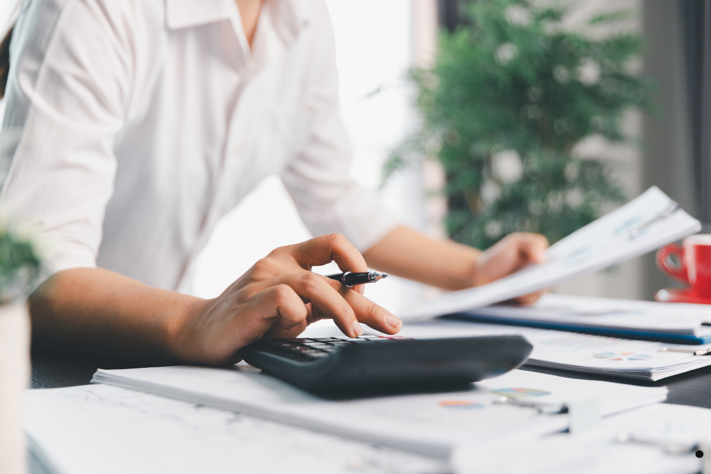 Person reviewing paperwork and using a calculator at a desk for business accounting.