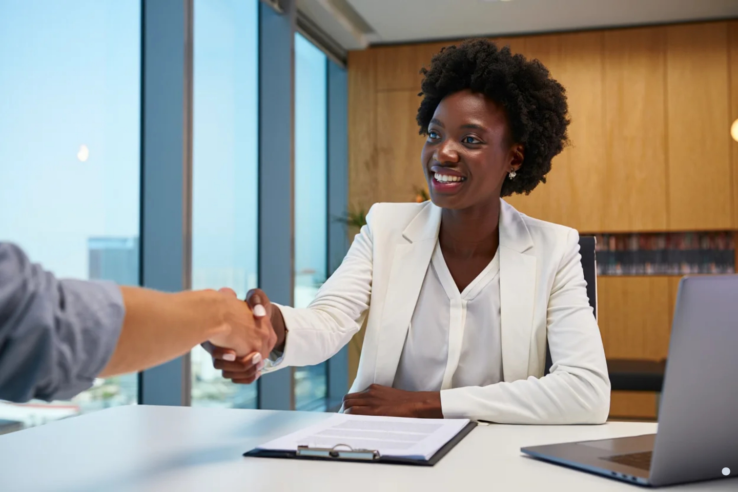 Smiling businesswoman shaking hands with a client across a desk.
