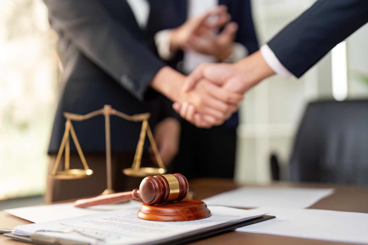 Business professionals shaking hands near a gavel and legal scales, symbolizing resolution of a surety bond or contractual matter.