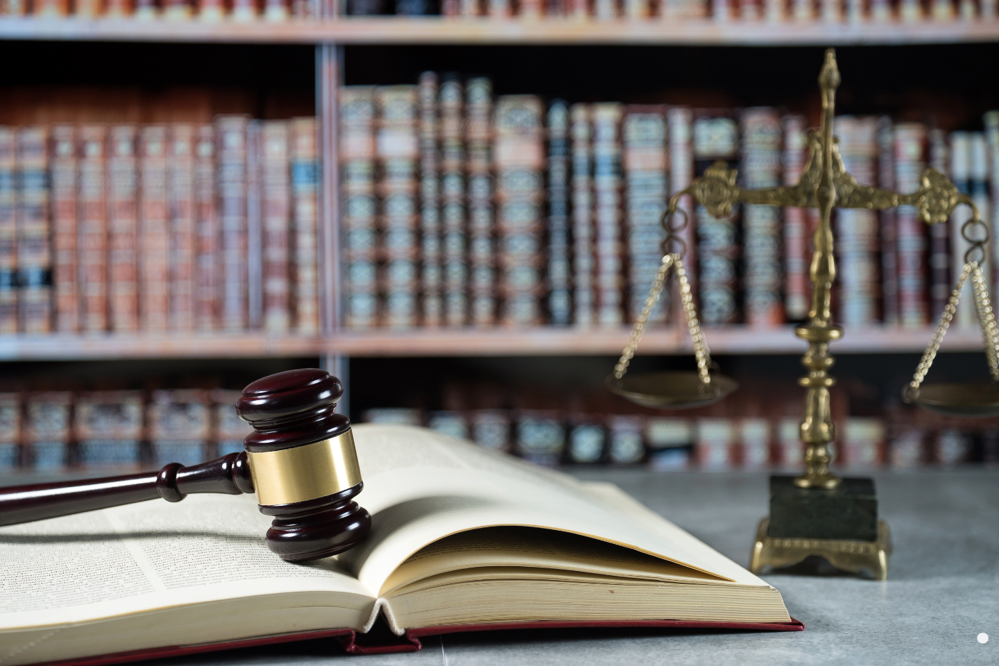 A gavel resting on an open law book beside a brass justice scale in a law library.