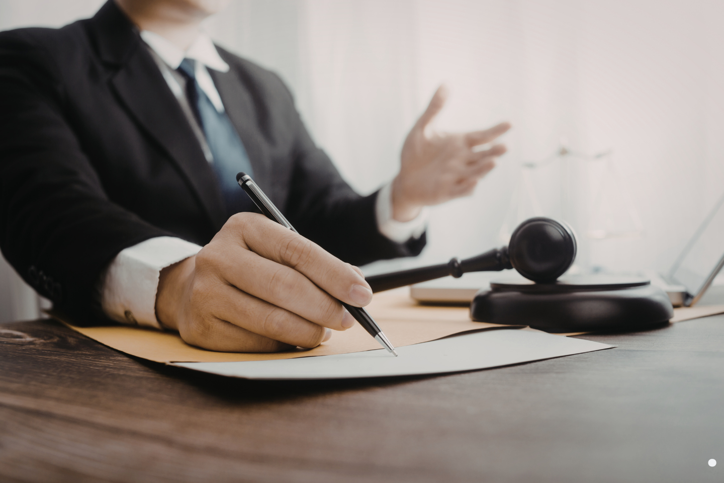 An attorney writing on legal documents at a desk with a gavel nearby.