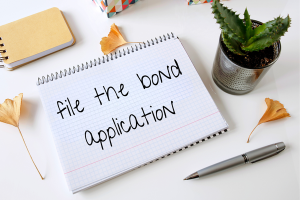 Notepad with the words 'File the Bond Application,' emphasizing the bond application process in Oklahoma for businesses needing license and permit bonds.